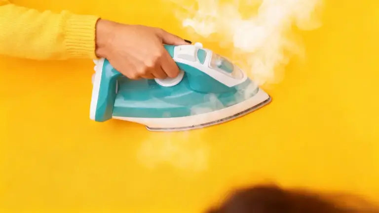 Mano che tiene un ferro da stiro a vapore acceso su sfondo giallo