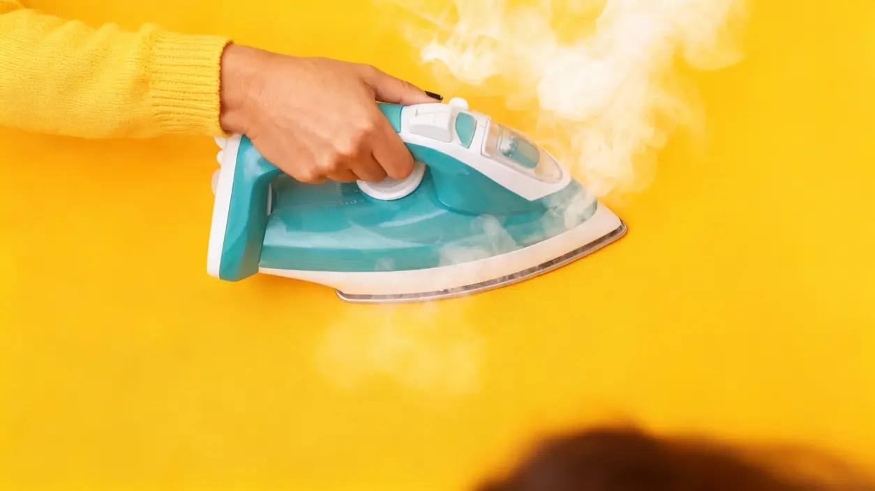 Mano che tiene un ferro da stiro a vapore acceso su sfondo giallo