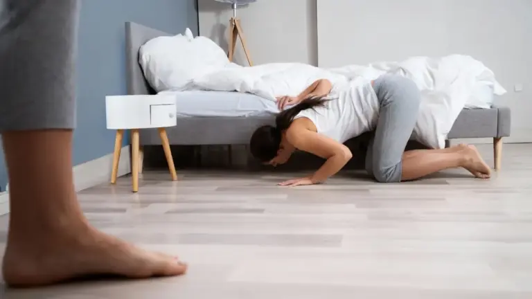 Persona inginocchiata che guarda sotto un letto in una camera da letto moderna
