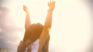 Una bambina con le braccia alzate verso il sole in una giornata luminosa