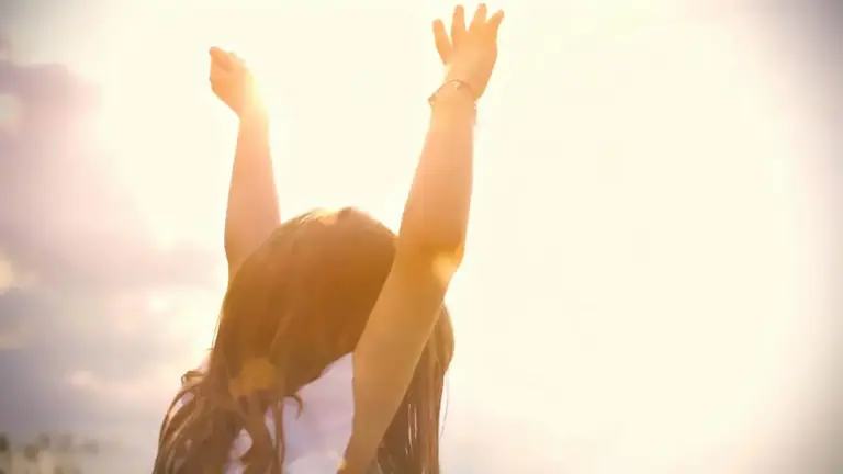 Una bambina con le braccia alzate verso il sole in una giornata luminosa