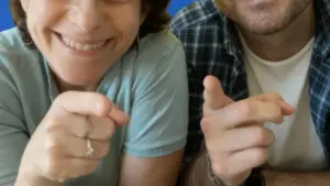 Due persone sorridenti indicano verso la fotocamera in atteggiamento amichevole