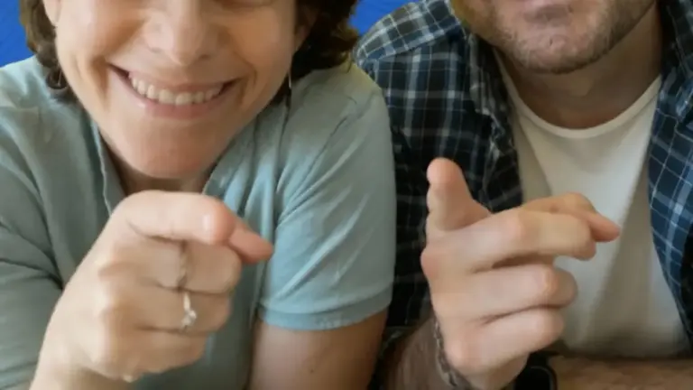 Due persone sorridenti indicano verso la fotocamera in atteggiamento amichevole