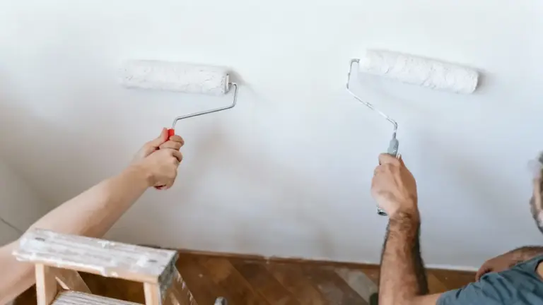 Due persone imbiancano una parete utilizzando rulli da pittura