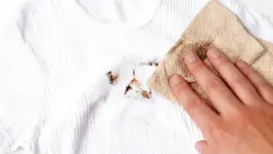 Mano che pulisce una macchia marrone su un tessuto bianco con un panno