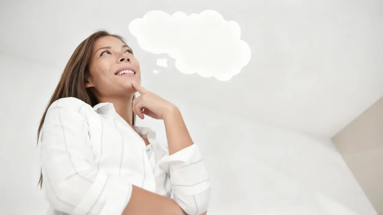 Persona sorridente con espressione pensierosa guarda in alto in una stanza luminosa