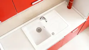 Lavello bianco con rubinetto cromato su piano cucina con ante rosse