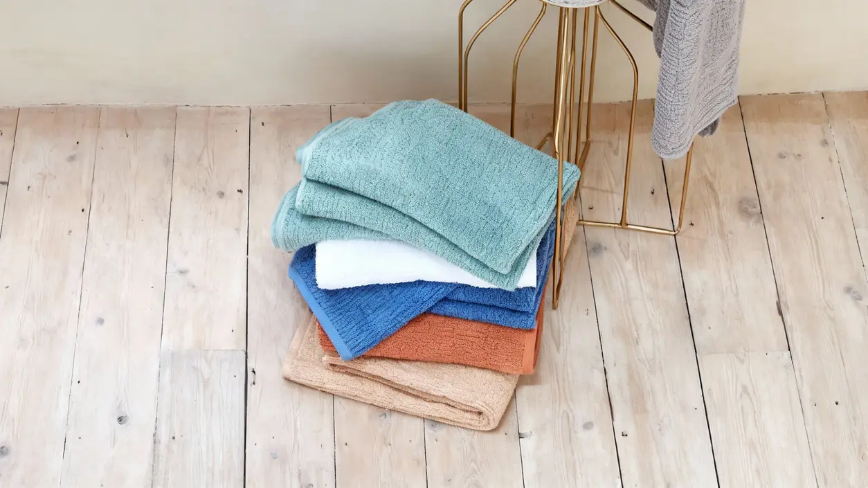 Pile di asciugamani colorati piegati su un pavimento in legno chiaro
