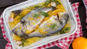 Due orate al forno condite con agrumi, aglio e rosmarino in una teglia