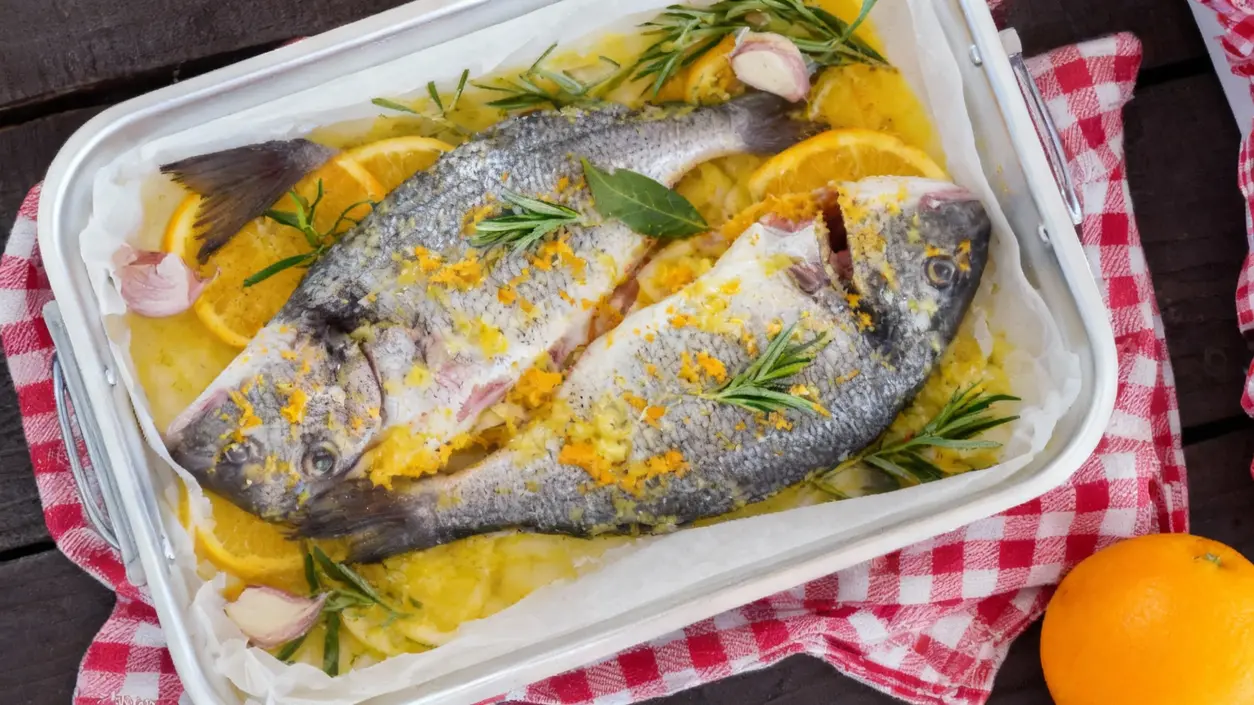 Due orate al forno condite con agrumi, aglio e rosmarino in una teglia