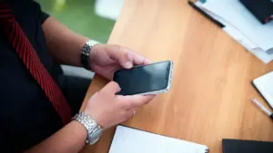 Persona tiene in mano uno smartphone su una scrivania con documenti