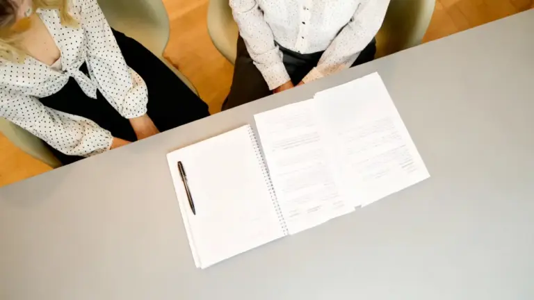 Due persone davanti a documenti e penna su un tavolo, in un contesto formale