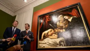 Due uomini in abiti eleganti accanto a un dipinto antico esposto su una parete colorata