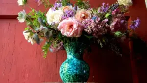 Bouquet di fiori estivi colorati in un vaso verde su sfondo di legno rosso