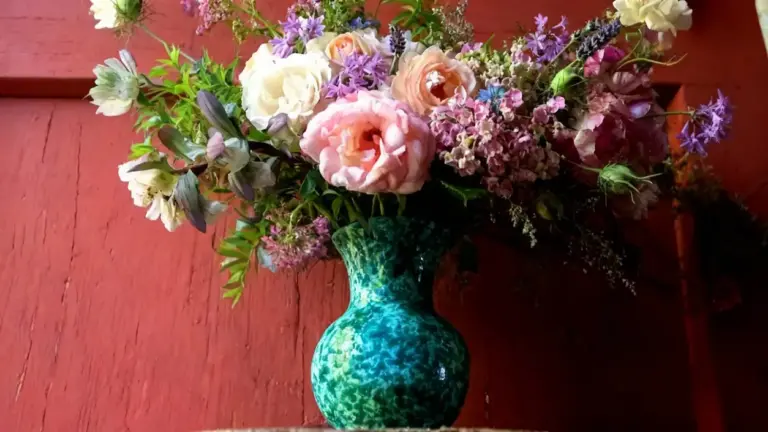 Bouquet di fiori estivi colorati in un vaso verde su sfondo di legno rosso