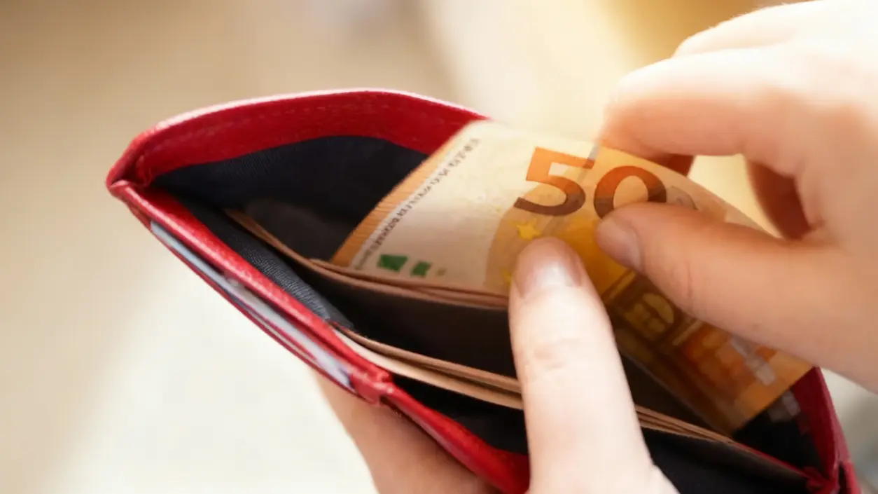Una mano prende una banconota da 50 euro da un portafoglio rosso